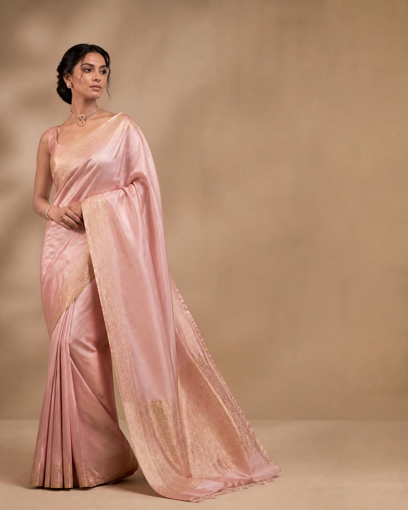 Model draped in a blush pink silk saree with gold zari border